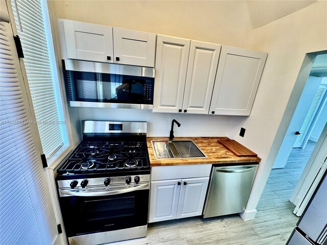 4710 Pine Tree Dr Unit 31, Miami Beach, FL 33140 - kitchen featuring stainless steel appliances, butcher block countertops, a sink, white cabinets, and lofted ceiling