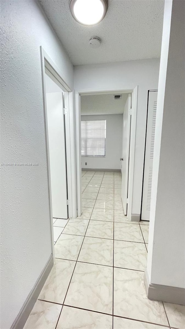 hall with a textured ceiling and baseboards