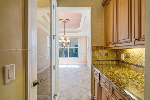 9192 Nugent Trl, West Palm Beach, FL 33411 - kitchen featuring ornamental molding, a chandelier, brown cabinetry, backsplash, and a tray ceiling