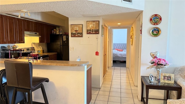 kitchen featuring electric stove, under cabinet range hood, freestanding refrigerator, light tile patterned flooring, and a peninsula