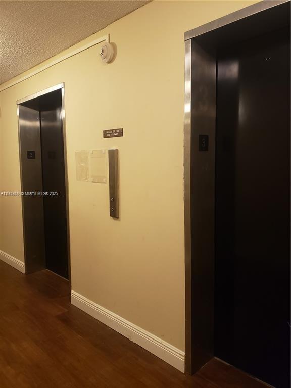 800 NE 195th St Unit 720, Miami, FL 33179 - corridor featuring elevator, dark wood-type flooring, a textured ceiling, and baseboards