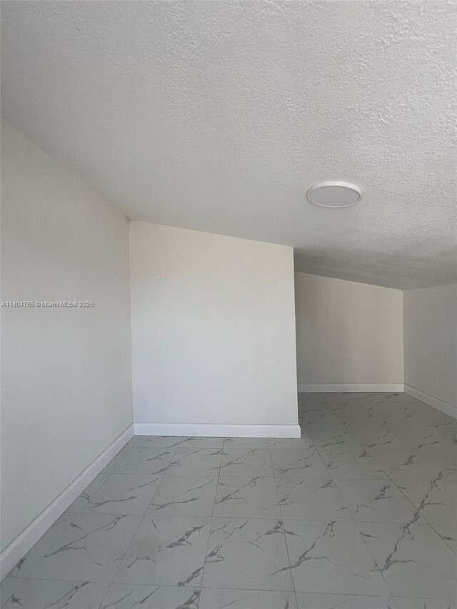 18740 NW 42nd Pl, Miami Gardens, FL 33055 - unfurnished room featuring baseboards, marble look tiles, and a textured ceiling