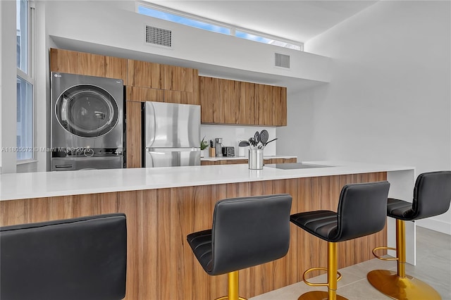 2345 SW 16th St, Miami, FL 33145 - kitchen featuring stacked washer / dryer, freestanding refrigerator, brown cabinets, light countertops, and a breakfast bar