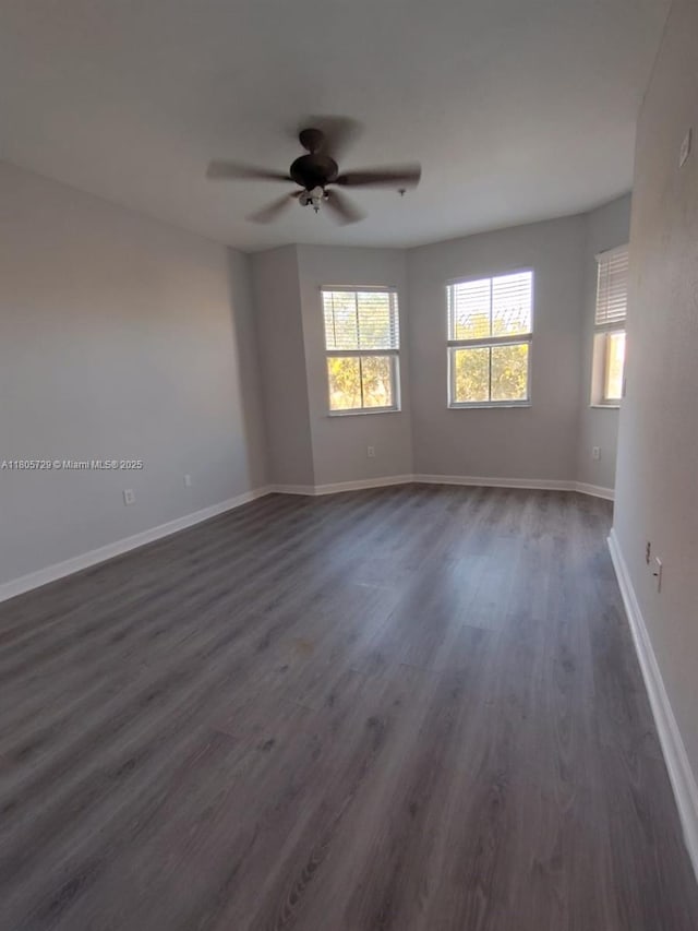 spare room featuring plenty of natural light, dark wood finished floors, baseboards, and a ceiling fan