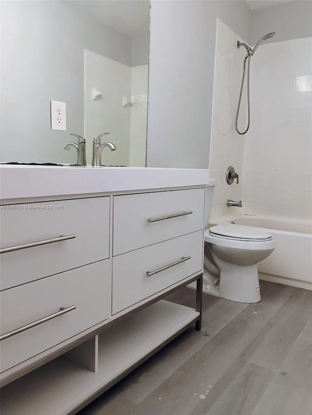 bathroom featuring wood finished floors, toilet, vanity, and tub / shower combination