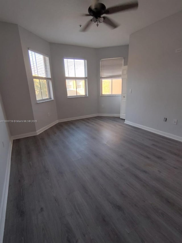 empty room with plenty of natural light, ceiling fan, dark wood-type flooring, and baseboards