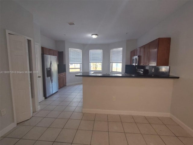 kitchen with stainless steel appliances, dark countertops, a peninsula, baseboards, and light tile patterned floors