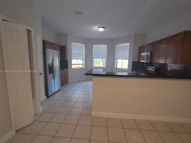 kitchen with appliances with stainless steel finishes, dark countertops, a peninsula, light tile patterned floors, and baseboards