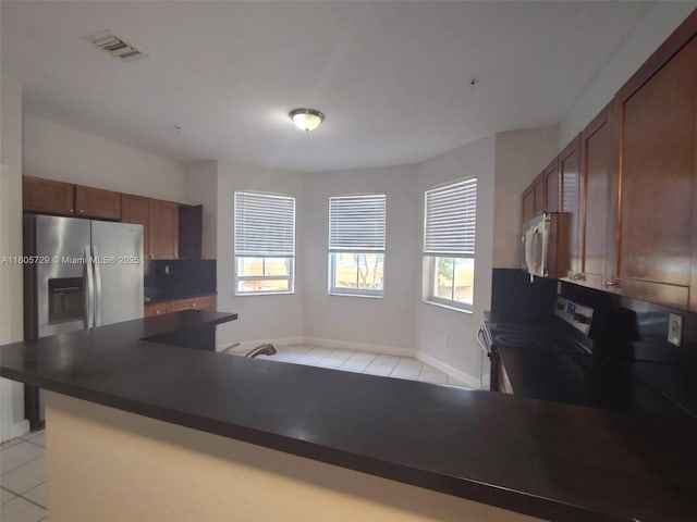 kitchen with appliances with stainless steel finishes, light tile patterned floors, dark countertops, and baseboards