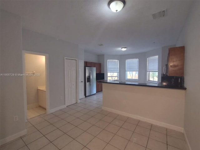 kitchen featuring stainless steel refrigerator with ice dispenser, dark countertops, a peninsula, and baseboards