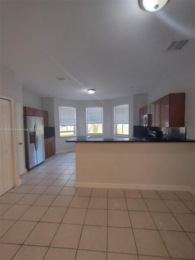 kitchen featuring stainless steel appliances, dark countertops, a peninsula, and plenty of natural light