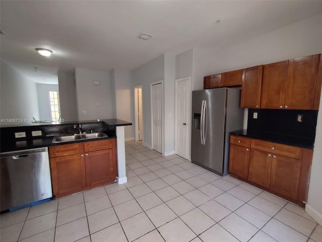 kitchen featuring stainless steel appliances, a sink, dark countertops, brown cabinetry, and baseboards