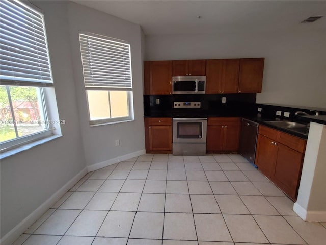 kitchen featuring stainless steel appliances, dark countertops, brown cabinetry, and a sink