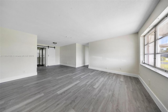 empty room featuring a barn door, wood finished floors, and baseboards