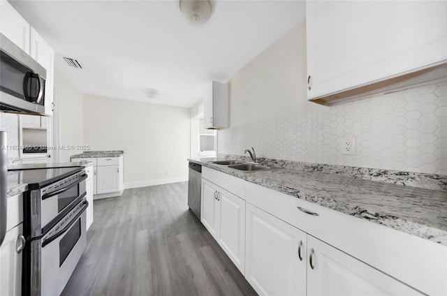 kitchen with a sink, stainless steel appliances, wood finished floors, tasteful backsplash, and white cabinets