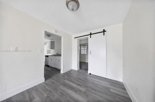 spare room featuring a barn door, baseboards, a sink, and dark wood-style flooring