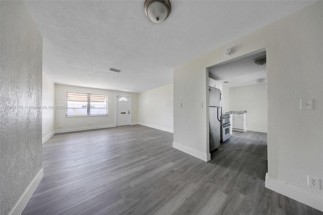 unfurnished living room with dark wood-type flooring, baseboards, a textured wall, and a textured ceiling