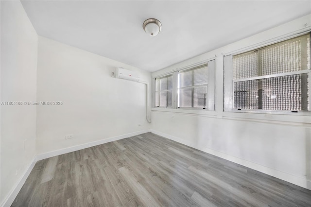 unfurnished room featuring a wall mounted air conditioner, wood finished floors, and baseboards