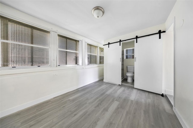 empty room featuring a barn door, wood finished floors, and baseboards