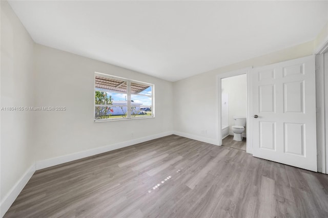 unfurnished bedroom with wood finished floors, baseboards, and connected bathroom