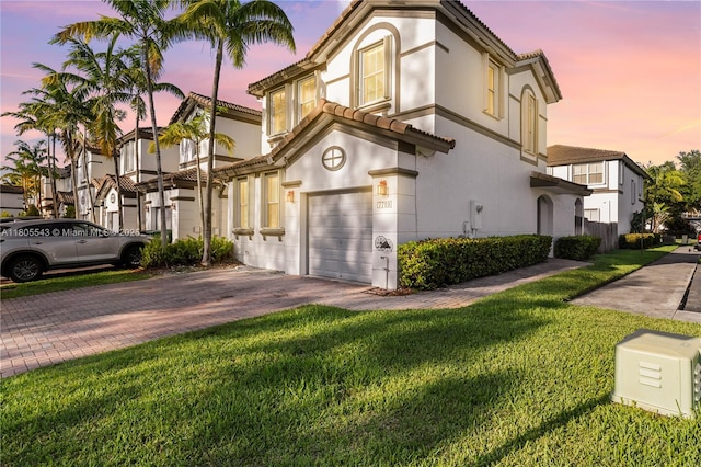 view of front facade with a tiled roof, decorative driveway, stucco siding, and a yard