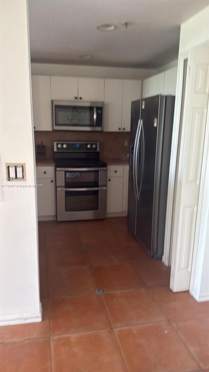 kitchen featuring stainless steel appliances, light tile patterned flooring, and white cabinets