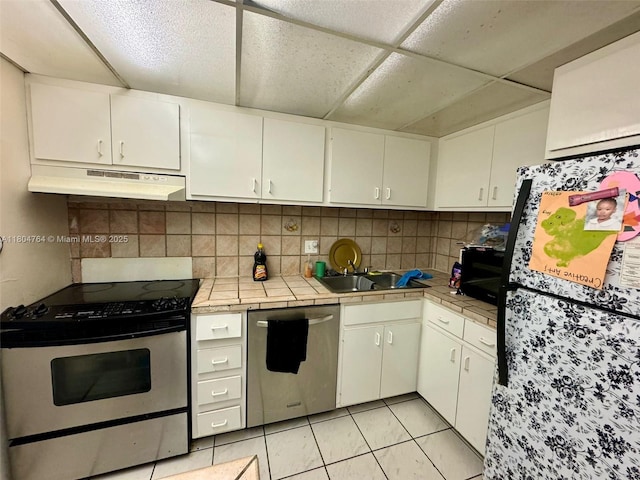 3660 Inverrary Dr Unit 2W, Lauderhill, FL 33319 - kitchen with under cabinet range hood, stainless steel appliances, tile countertops, white cabinetry, and decorative backsplash