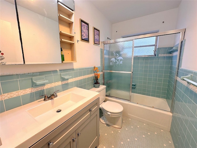 bathroom featuring tile walls, tile patterned flooring, toilet, combined bath / shower with glass door, and vanity