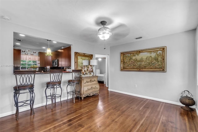 kitchen with dark wood-style flooring, dark countertops, a ceiling fan, baseboards, and stainless steel microwave