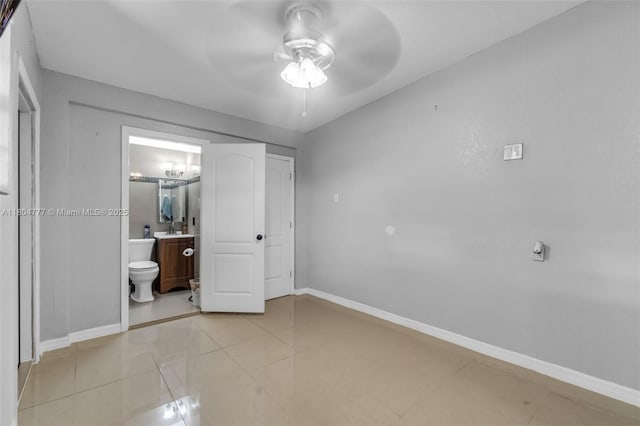 unfurnished bedroom featuring baseboards, connected bathroom, a sink, a ceiling fan, and light tile patterned floors