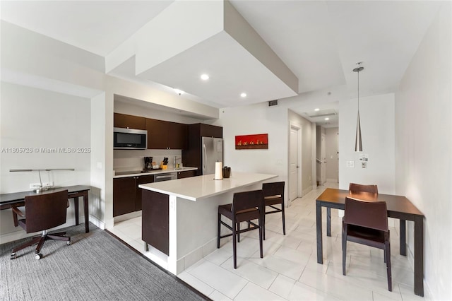 kitchen featuring appliances with stainless steel finishes, dark brown cabinetry, a kitchen bar, light countertops, and a kitchen island