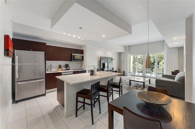 kitchen featuring appliances with stainless steel finishes, light countertops, a breakfast bar, a sink, and dark brown cabinets