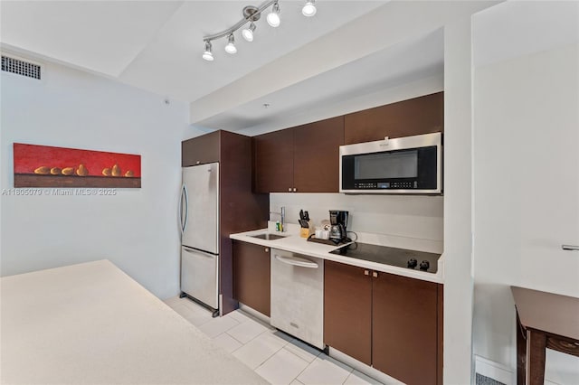 kitchen with appliances with stainless steel finishes, dark brown cabinetry, light tile patterned floors, light countertops, and a sink