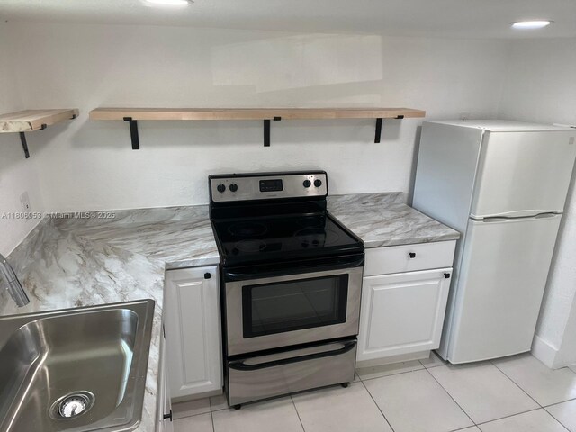 126 NW 13th Ave, Dania Beach, FL 33004 - kitchen featuring freestanding refrigerator, stainless steel electric range, a sink, white cabinetry, and light tile patterned flooring