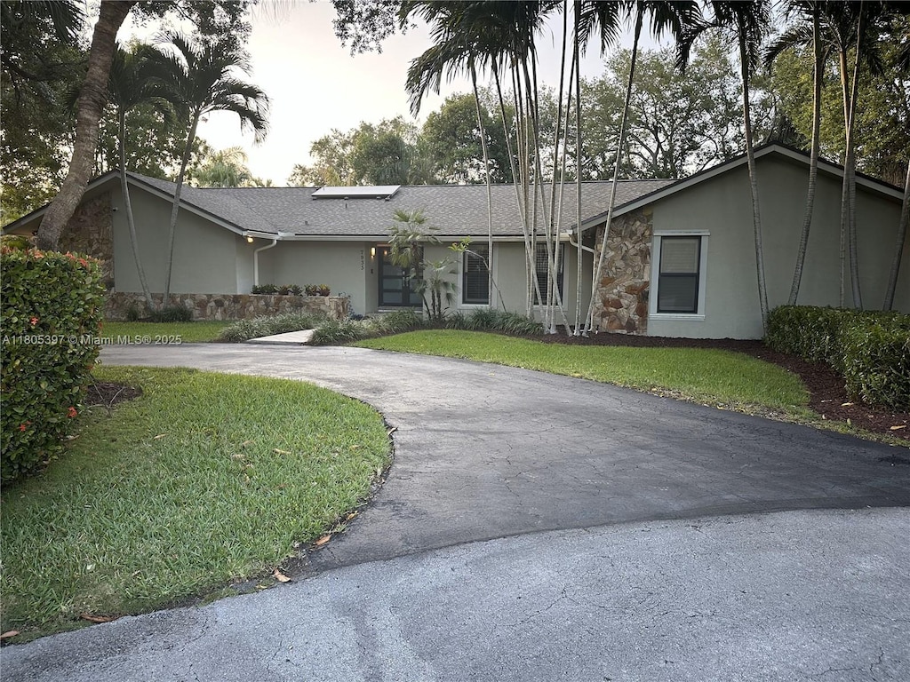 view of front of house with stucco siding, curved driveway, stone siding, and a front yard