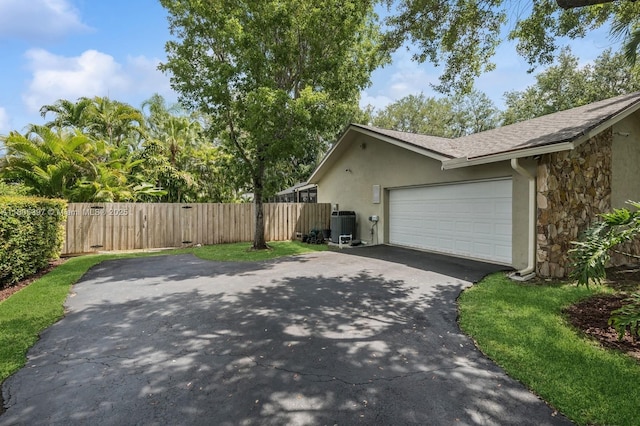 7935 SW 155th St, Palmetto Bay, FL 33157 - view of property exterior with driveway, stucco siding, stone siding, central AC, and roof with shingles