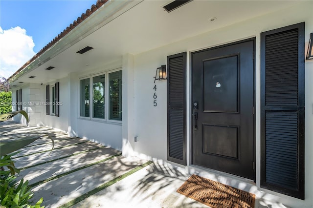 view of exterior entry with stucco siding, a tiled roof, and a porch