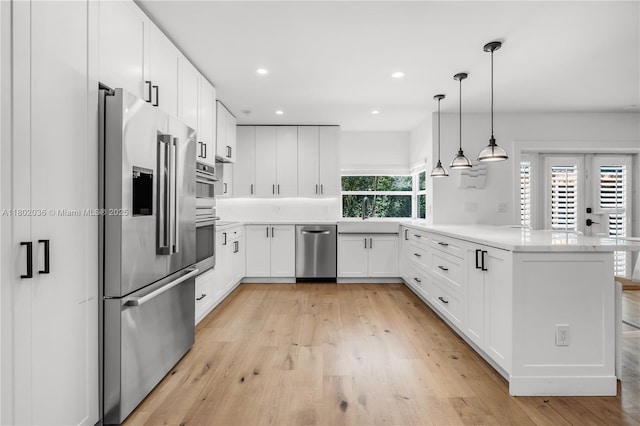 kitchen with appliances with stainless steel finishes, a peninsula, light countertops, light wood-type flooring, and white cabinets