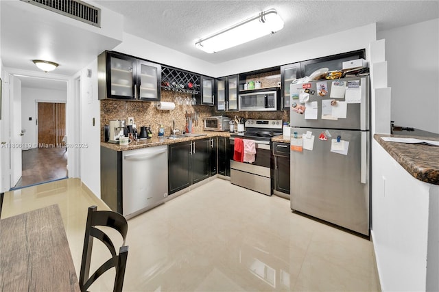 kitchen featuring stainless steel appliances, tasteful backsplash, a textured ceiling, open shelves, and glass insert cabinets