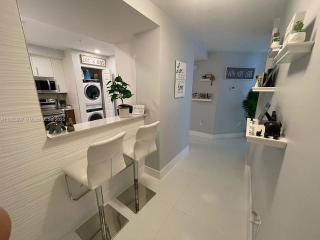 kitchen featuring stainless steel appliances, stacked washer and clothes dryer, light tile patterned floors, a breakfast bar area, and white cabinets
