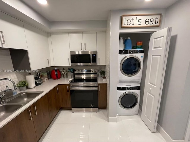 kitchen with stainless steel appliances, stacked washing machine and dryer, a sink, white cabinets, and light countertops