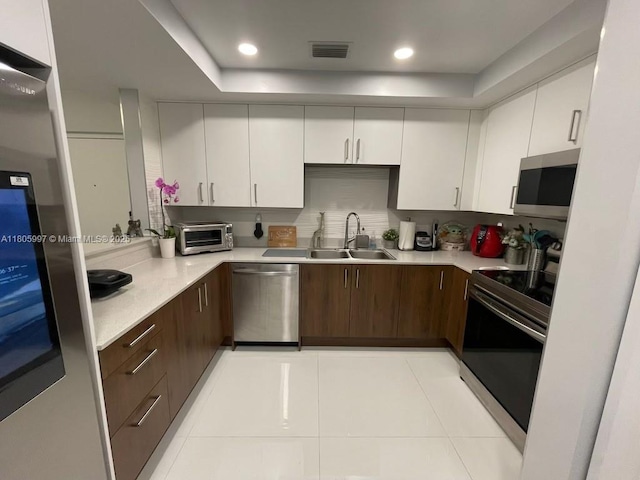 kitchen featuring appliances with stainless steel finishes, a sink, light countertops, white cabinets, and light tile patterned floors