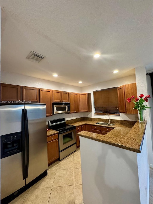 kitchen with appliances with stainless steel finishes, a sink, a peninsula, brown cabinets, and light tile patterned flooring