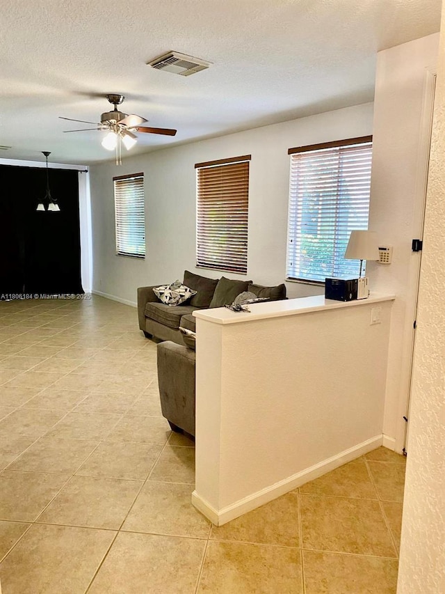 living room featuring light tile patterned floors, plenty of natural light, a textured ceiling, a ceiling fan, and baseboards