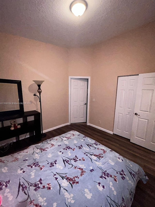 bedroom featuring dark wood finished floors, a textured ceiling, baseboards, and a closet