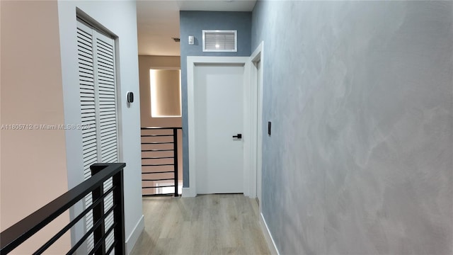 corridor with light wood-style floors, an upstairs landing, and baseboards