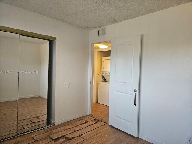 8620 N Sherman Cir Unit 202, Miramar, FL 33025 - unfurnished bedroom featuring stacked washer / drying machine, light wood-style flooring, a closet, a textured ceiling, and baseboards