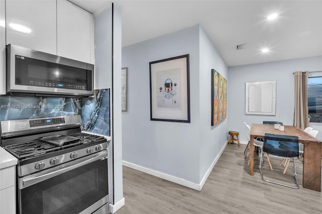 1635 NE 174th St, North Miami Beach, FL 33162 - kitchen with appliances with stainless steel finishes, white cabinetry, light wood-style flooring, baseboards, and tasteful backsplash