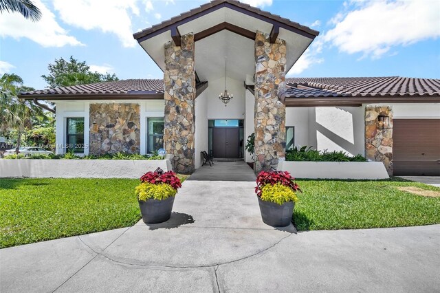 11850 SW 42nd Ct, Davie, FL 33330 - property entrance featuring a tile roof, stone siding, a lawn, stucco siding, and an attached garage