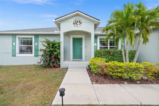 7434 Ashtabula St, Englewood, FL 34224 - doorway to property featuring a shingled roof, a lawn, and stucco siding